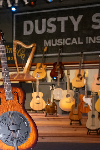 Resonator guitar with an assortment of other fretted instruments and a harp behind