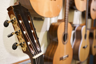 Close-up of a nylon-strung guitar headstock with other guitars in the background