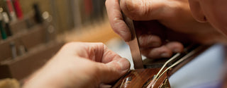 Close-up of hands holding a chisel against a guitar headstock