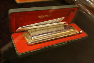 Hohner chromatic harmonica in an open red case on a dark surface