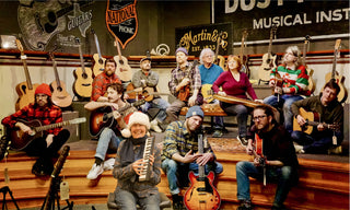 12 people with instruments sitting on the Dusty Strings stage